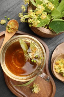 Lezzetli ıhlamur çayı fincanda, kaşıkta, yapraklarda ve çiçeklerde koyu dokulu masada, düz yerde.