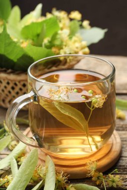 Fincanda lezzetli ıhlamur çayı, ahşap masada yapraklar ve çiçekler koyu arka planda, yakın plan.