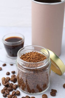 Kavanozlarda hazır kahve, fasulye ve sıcak içecek açık gri masada, yakın plan.