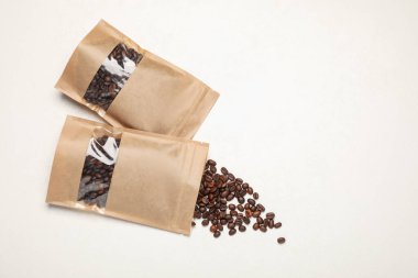 Fermuarlı stand-up paketleri ve kahve çekirdekleri beyaz masada, düz yerde. Tasarım için model