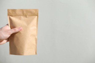 Açık gri arka planda fermuarlı stand-up çantası tutan kadın, yakın plan. Metin için boşluk