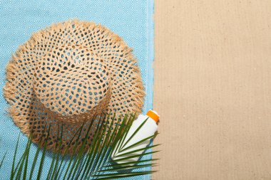 Plaj havlusu, hasır şapka, güneş kremi ve dışarıda kum üzerinde palmiye yaprağı. Metin için boşluk