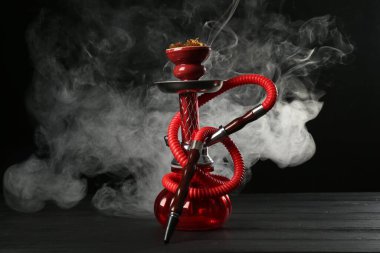 Siyah arka planda duman olan ahşap masada nargile.