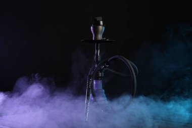 Siyah arka planda sigara dumanı olan ahşap masada nargile.