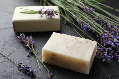 Aromatik sabun barları ve lavanta çiçekleri koyu dokulu masa üzerinde, yakın plan.
