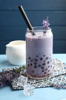 Lezzetli sütlü çay bardakta ve lavanta çiçekleri açık mavi ahşap masada, yakın plan.