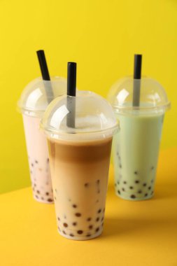 Sarı arka planda plastik bardakta lezzetli süt köpüğü çayı.