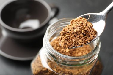 Koyu renkli masada kaşıktan kavanoza granüle kahve ekliyorum.