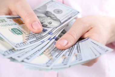 Açık gri arka planda dolar banknotları sayan kadın, yakın plan