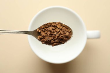 Bej arka planda fincanın üzerinde hazır kahve ile kaşık, üst görünüm