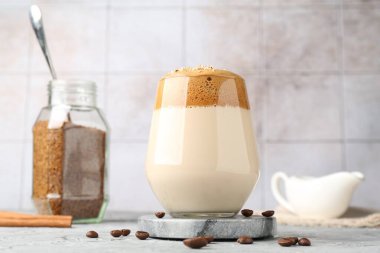 Bardakta lezzetli dalgona kahvesi, fasulye, granüller ve gri masada tarçın, düşük açı.