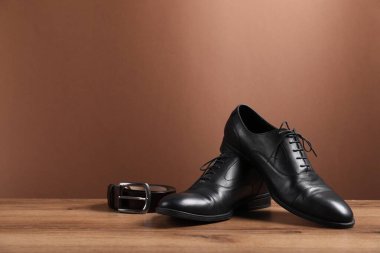 Bir çift siyah deri ayakkabı ve kemer ahşap zemin üzerinde kahverengi arkaplan, metin için boşluk