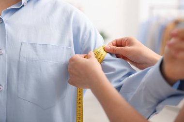 Atölyede bantla kadının kolunu ölçen terzi, yakın plan.