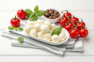 Lezzetli mozzarella peyniri, domates, fesleğen ve baharatlar beyaz ahşap masada, yakın plan.