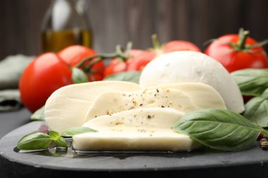 Lezzetli mozzarella peyniri, domates, fesleğen ve baharatlar masada, yakın plan.