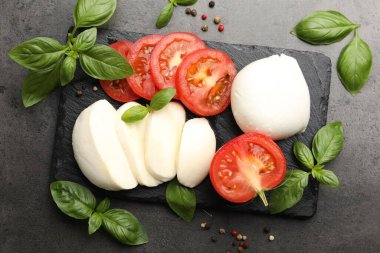 Lezzetli mozzarella peyniri, domates, fesleğen ve biberler gri masada, düz yerde.