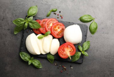 Lezzetli mozzarella peyniri, domates, fesleğen ve biberler gri masada, düz yerde.