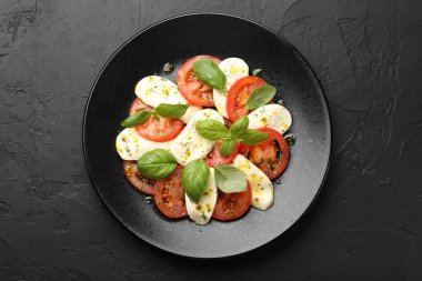 Peynirli Caprese salatası, domates, fesleğen ve baharatlar siyah masada.