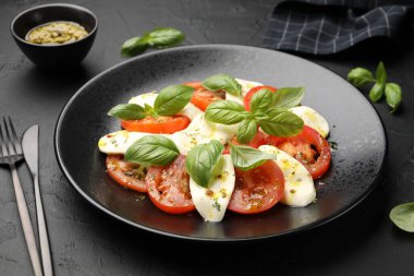 Mozzarella, domates, fesleğen ve baharatlarla siyah masaya yakın plan Caprese salatası.