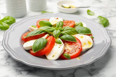 Beyaz mermer masada mozarella, domates, fesleğen ve baharatlı Caprese salatası.