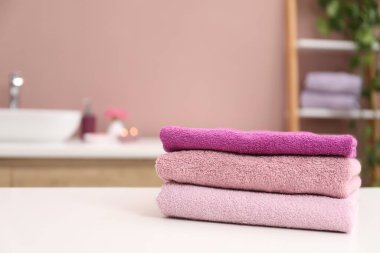 Banyodaki beyaz masanın üzerine renkli havlular yığılmış, yakın plan. Metin için boşluk