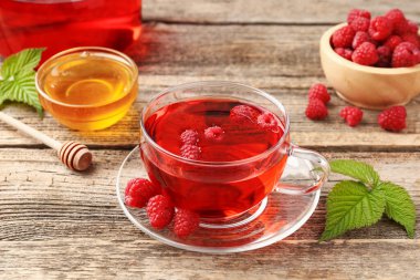 Lezzetli ahududu çayı, böğürtlen ve yapraklar ahşap masada, yakın plan.