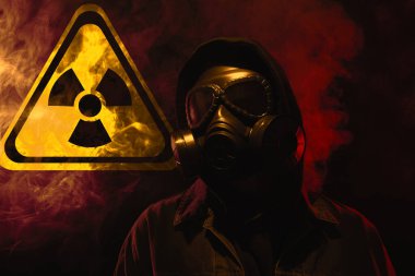 Siyah arka planda duman içinde gaz maskesi takan adam. Arkasında radyoaktif bir işaret var.