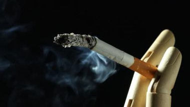Siyah arka planda yanan sigaralı ahşap el figürü, yakın plan.
