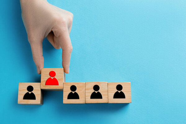 Dismissal. Woman taking cube with red human icon among others with black ones on light blue background, top view