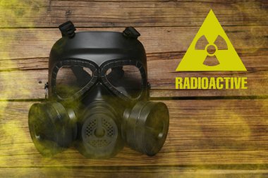 Radyasyon tehdidi. Gaz maskesi, radyoaktif tabela ve ahşap masada duman, üst manzara.