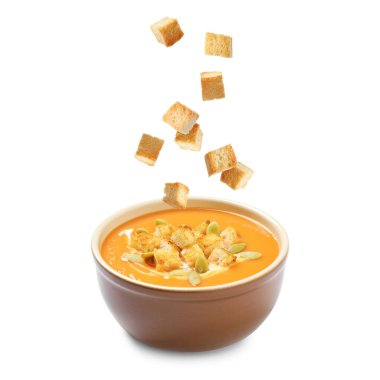 Beyaz arka planda kremalı balkabağı çorbasına düşen kızarmış ekmekler.