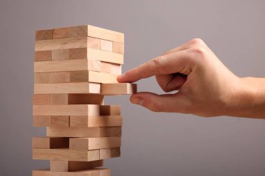Lviv, Ukrayna - 08 Aralık 2023: Jenga oynuyorum. Gri arkaplandaki tahta bloğu kuleden kaldıran adam, yakın plan