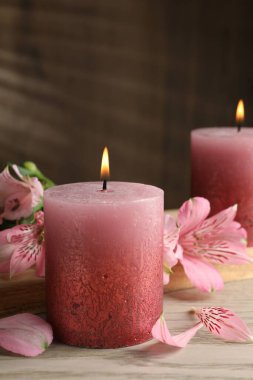 Beyaz ahşap masada yanan mumlar ve zambak çiçekleri, yakın plan.