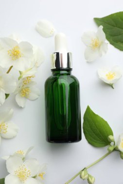 Temel yağ, yasemin çiçekleri ve beyaz arka planda yeşil yapraklar.