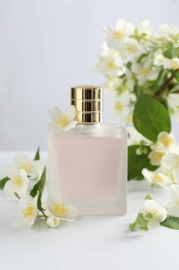 Beyaz masada bir şişe parfüm ve yasemin çiçeği.