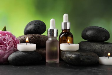 Islak taşlı spa kompozisyonu, kozmetik ürünleri ve koyu desenli masada yanan mumlar, bulanık yeşil arka plan, yakın çekim