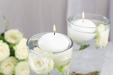 Mumları bardaklarda yakıyor, masada çiçekler ve suyla, yakın plan.