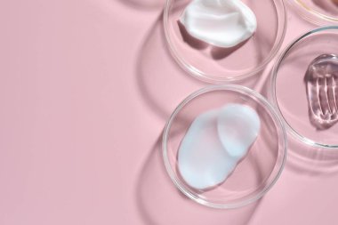 Petri kaplarında pembe arka planda farklı kozmetik ürünleri var. Metin için boşluk