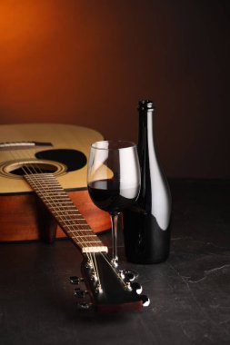 Akustik gitar ve kırmızı şarap siyah masada, kahverengi ışık, yakın plan.