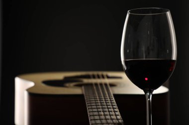 Akustik gitar ve siyah arka planda bir kadeh kırmızı şarap, yakın plan. Metin için boşluk