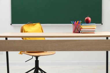 Farklı okul kırtasiyesi ve kırmızı elma, kapalı alanda tahtaya yakın ahşap masada.