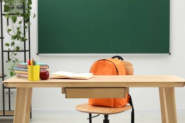 Farklı okul kırtasiyesi ve kırmızı elma, kapalı alanda tahtaya yakın ahşap masada.