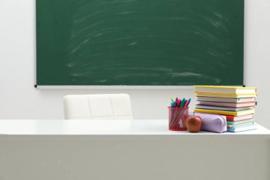 Farklı okul kırtasiyesi ve elma beyaz masada, kapalı alanda.