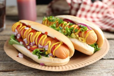 Ahşap masada soslu, marullu ve soğanlı lezzetli sosisliler, yakın plan.