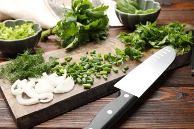 Farklı taze otlar, baharatlar ve bıçaklar ahşap masada, yakın plan.