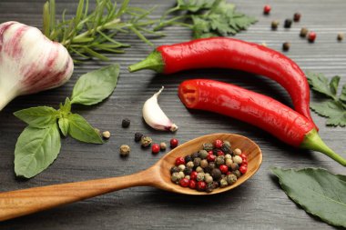 Farklı aromatik otlar, ürünler ve koyu ahşap masa üzerinde biberli kaşık, yakın plan.