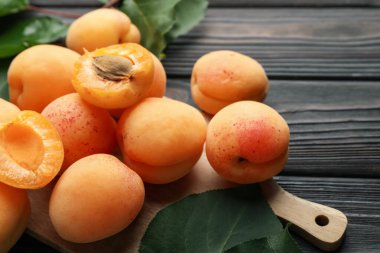 Taze kayısılar ve yeşil yapraklar koyu ahşap masada, yakın plan.