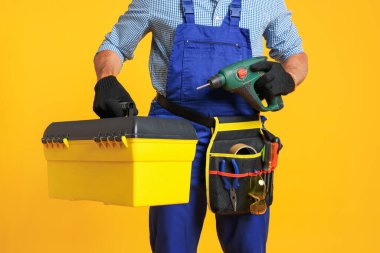 Turuncu arka planda alet kutusu ve elektrikli tornavidası olan profesyonel tamirci, yakın plan.