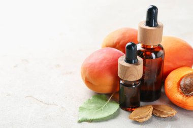 Şişeler dolusu gerekli yağ, taze kayısılar, çekirdekler ve açık gri masada yeşil yaprak, yakın plan. Metin için boşluk