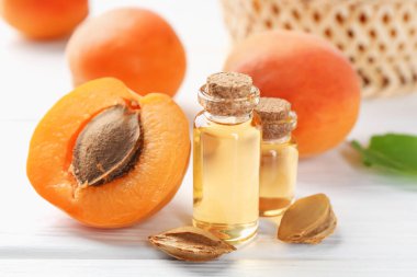 Beyaz ahşap masa üzerinde gerekli yağ şişeleri, taze kayısılar ve çekirdekler, yakın plan.